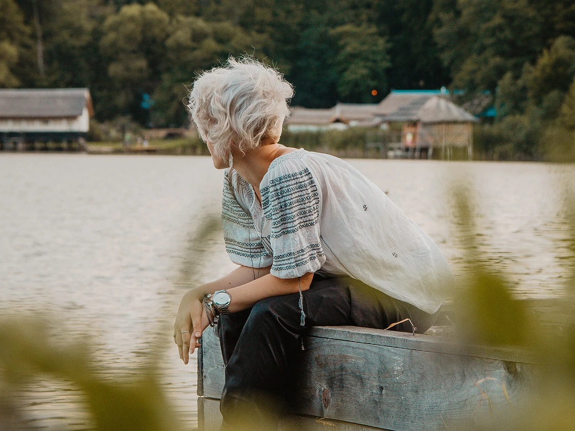 Frau sitzt am see und schaut hinaus